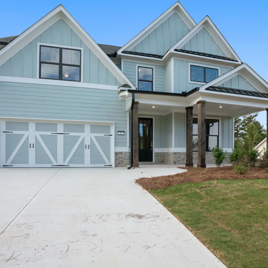 Modern two-story blue house with white trim, double garage, front porch, and landscaped yard under clear sky
