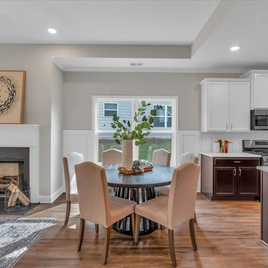 Modern dining area with a round table, beige chairs, fireplace, and white kitchen cabinets in an open floor plan.