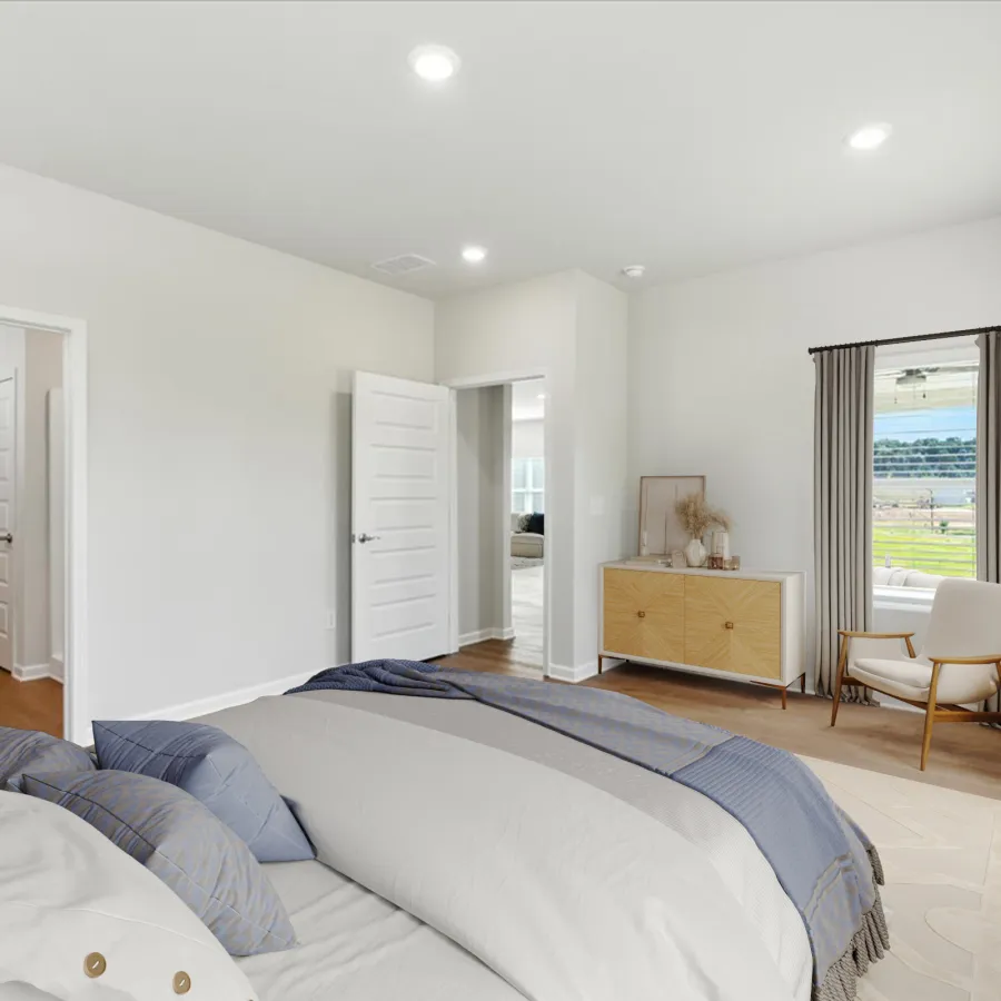 Bright modern bedroom with a large bed, wooden floor, window with curtains, and a chair by a side table.