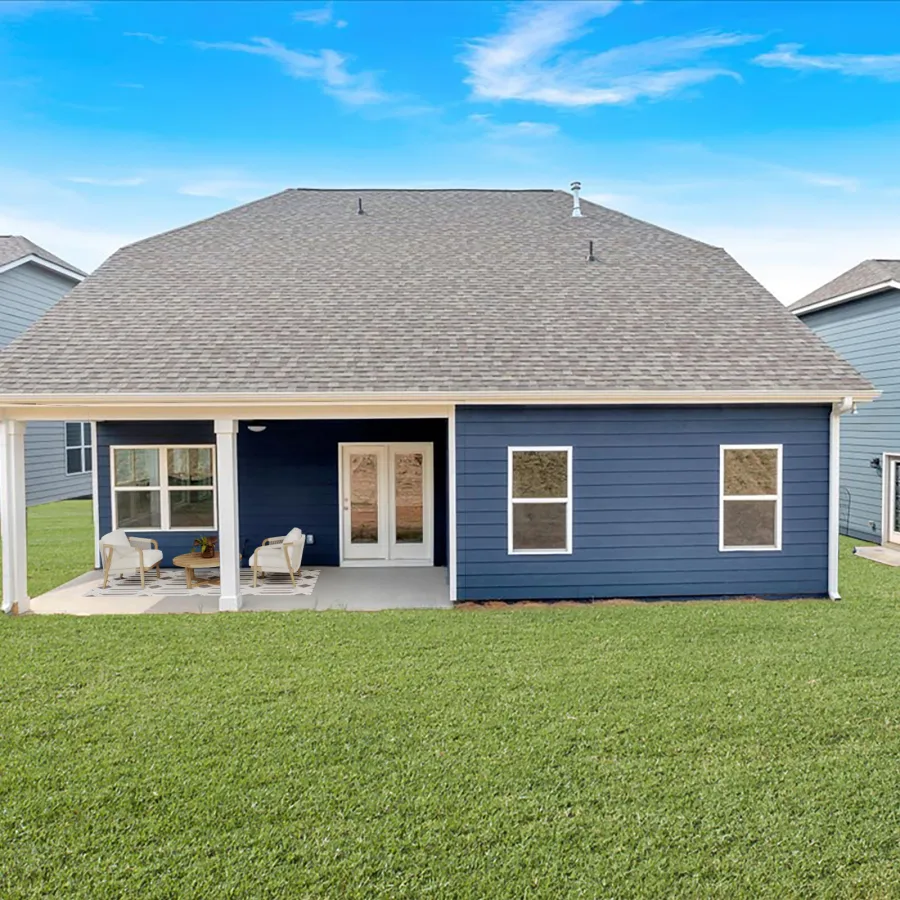 Modern blue house with covered patio and outdoor seating on a large green lawn under a clear sky