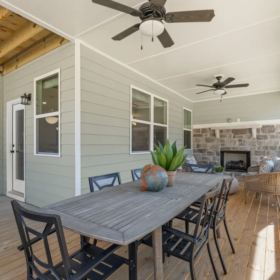 Spacious screened porch with wooden flooring, dining table, chairs, ceiling fans, and stone fireplace.