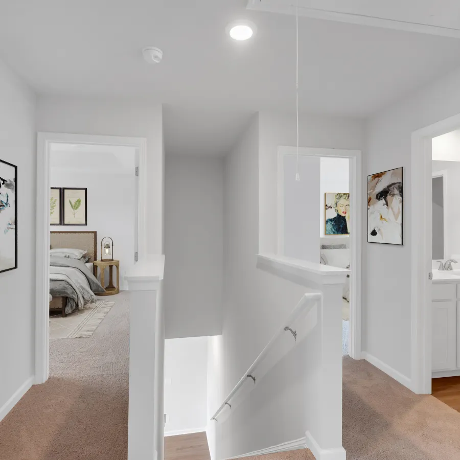 Bright hallway with carpeted floors, leading to bedrooms and a bathroom with modern decor and framed artwork.