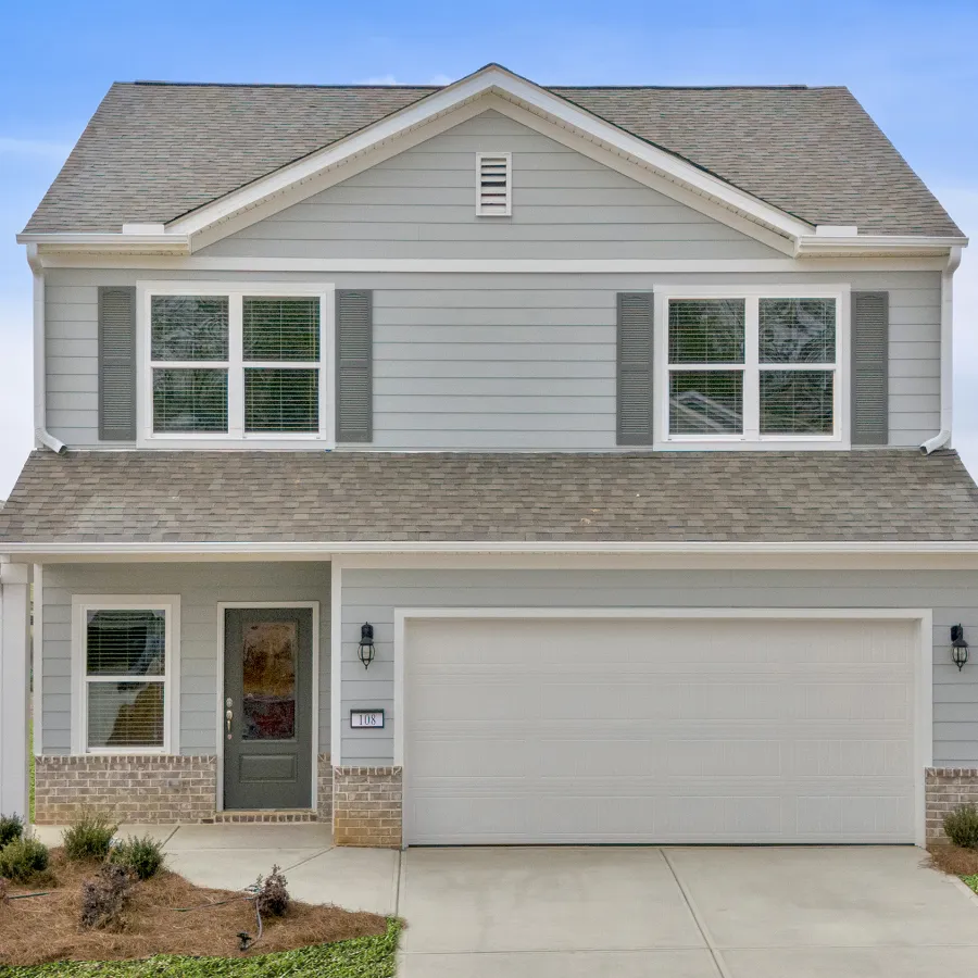 Two-story gray siding house with white trim, attached garage, landscaped front yard, and a pond in the background