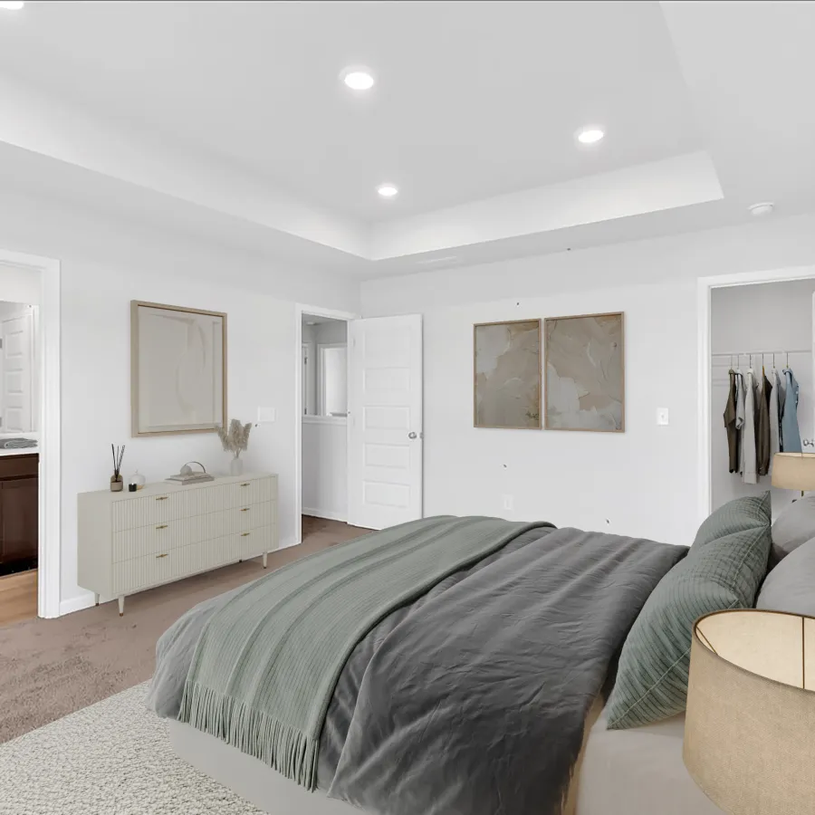 Modern bedroom with gray bedding, white walls, carpet flooring, dresser, framed art, and open doors to bathroom and closet.