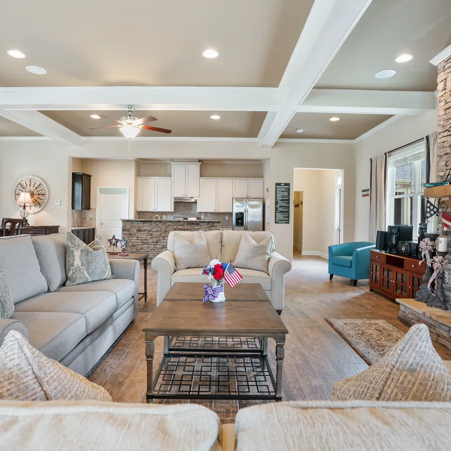 Spacious living room with light gray sofas, wooden coffee table, stone fireplace, and open kitchen in the background
