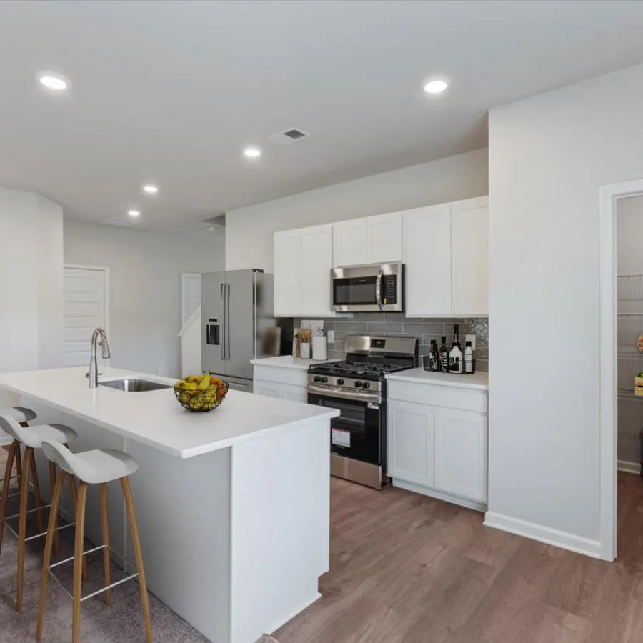 Modern white kitchen with island, stainless steel appliances, bar stools, and a stocked pantry with wooden shelves.