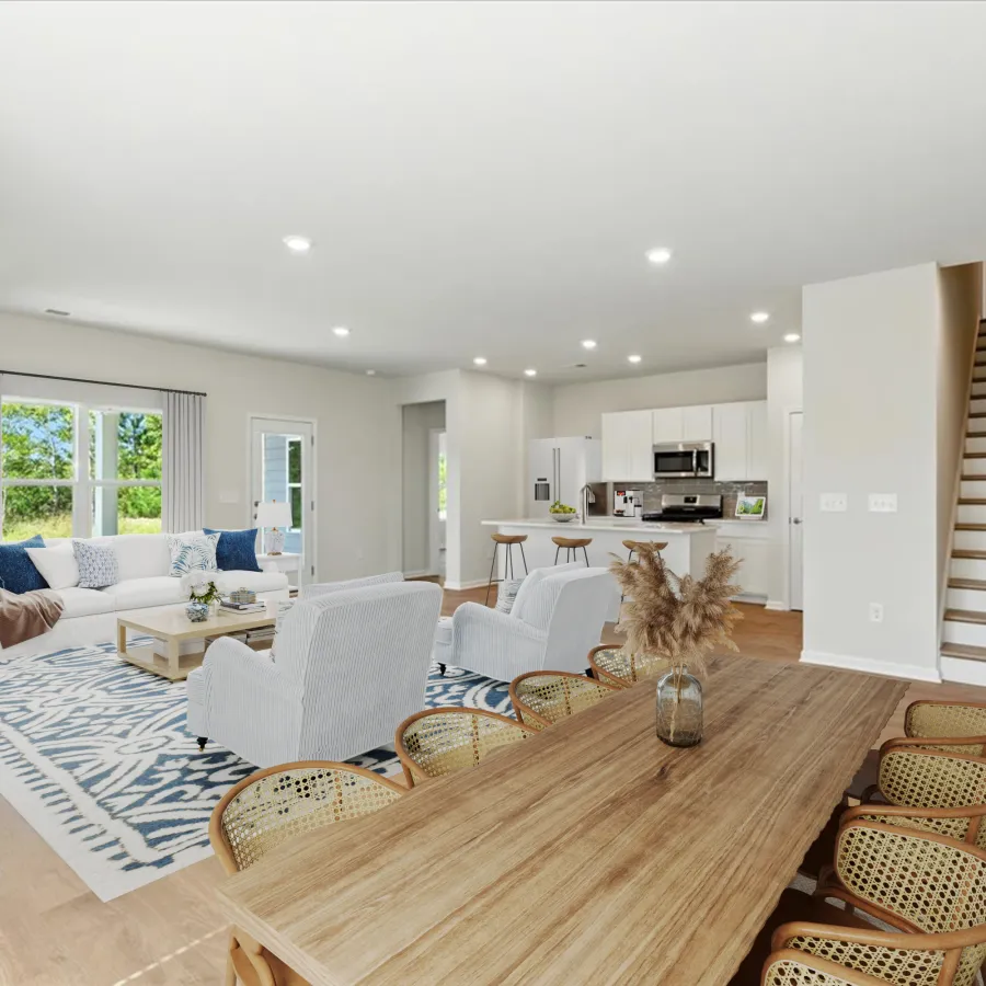 Bright open-concept living and dining area with modern kitchen, wooden table, wicker chairs, and soft blue accents.