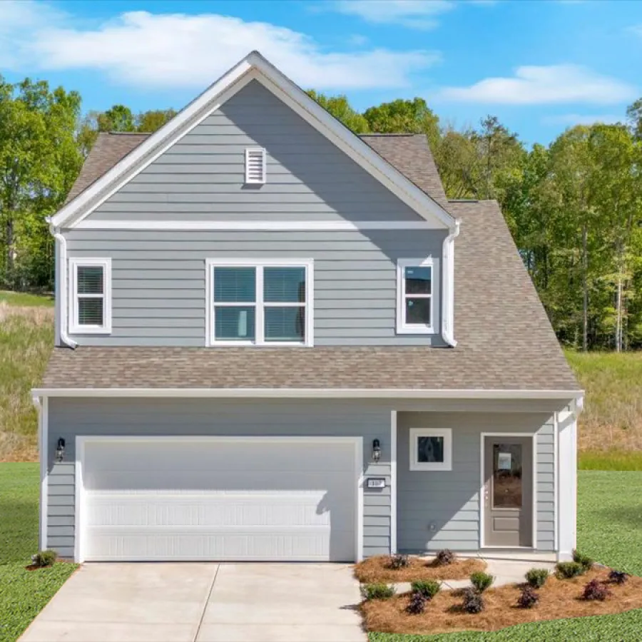 Two-story gray suburban house with a double garage, front door porch, and landscaped yard under a blue sky.