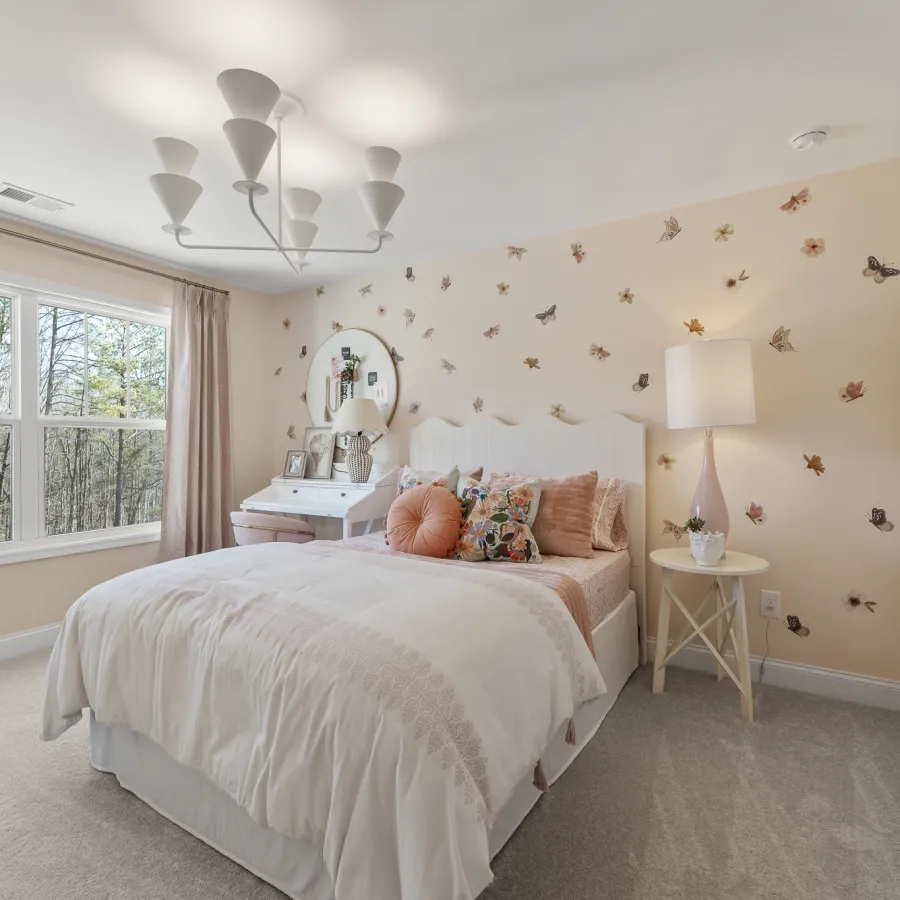 Cozy bedroom with white bed, floral pillows, butterfly wall decals, large window, and modern chandelier light fixture.