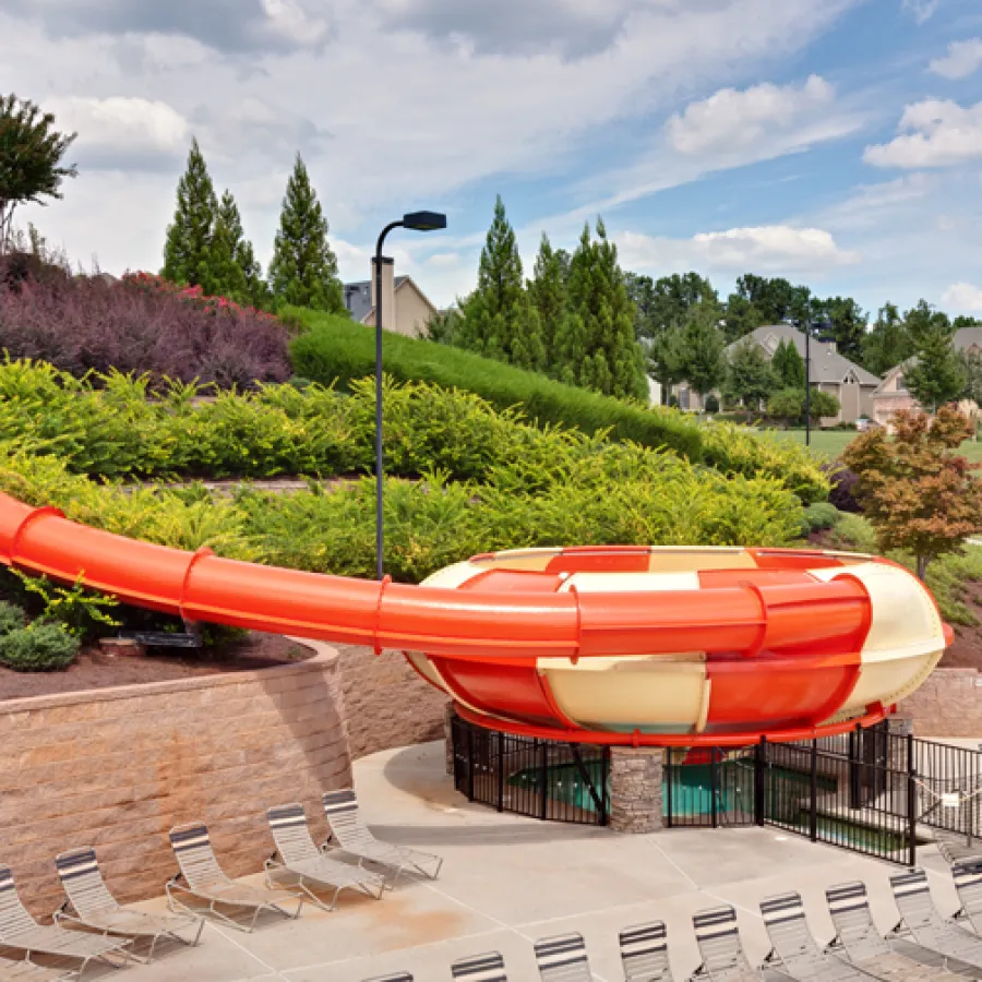 Large orange and white water slide with funnel shape at the bottom surrounded by lounge chairs and greenery.