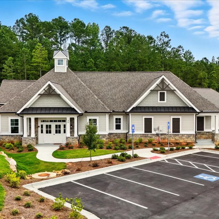 Modern community building with pitched roof, stone accents, landscaped garden, and empty parking lot in a wooded area