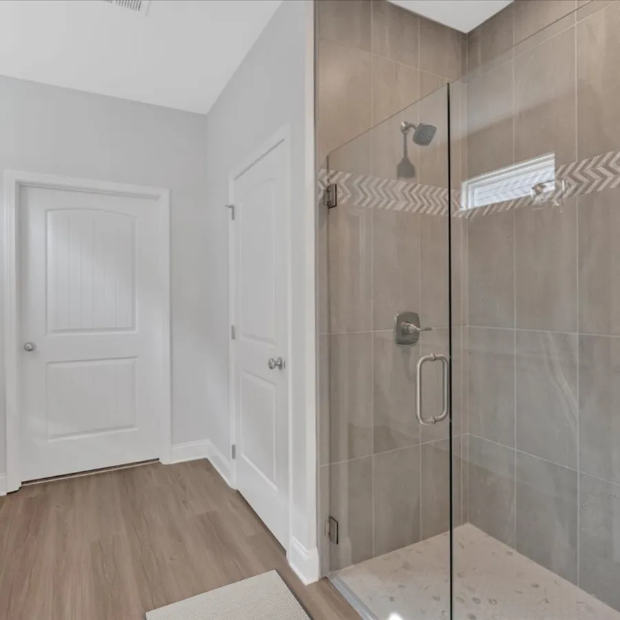 Modern bathroom with glass-enclosed shower, beige tiles, wooden floor, and white paneled doors.