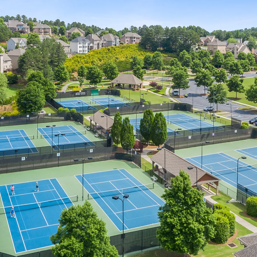 Aerial view of multiple blue tennis courts surrounded by greenery and residential homes on a sunny day
