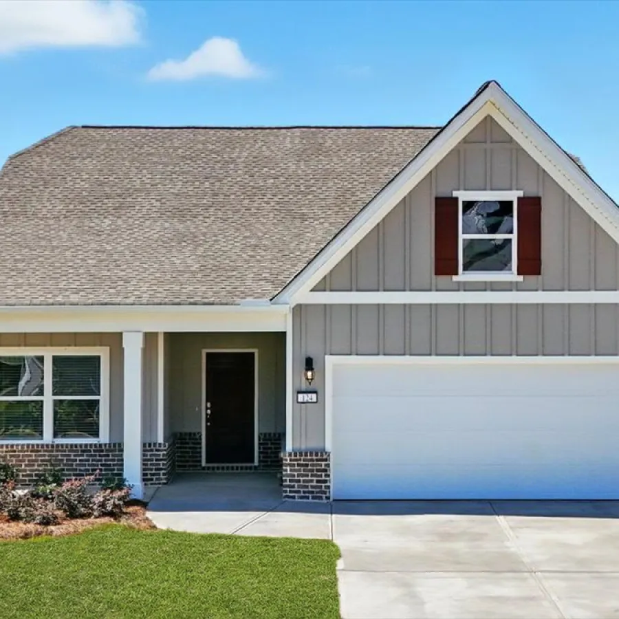 Modern single-story house with gray siding, brick accents, white garage door, and green lawn under a blue sky.