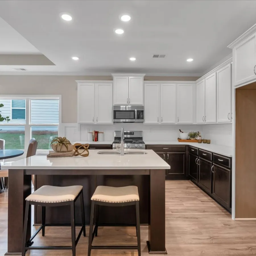 Modern kitchen with white upper cabinets, dark lower cabinets, island with stools, and hardwood floors
