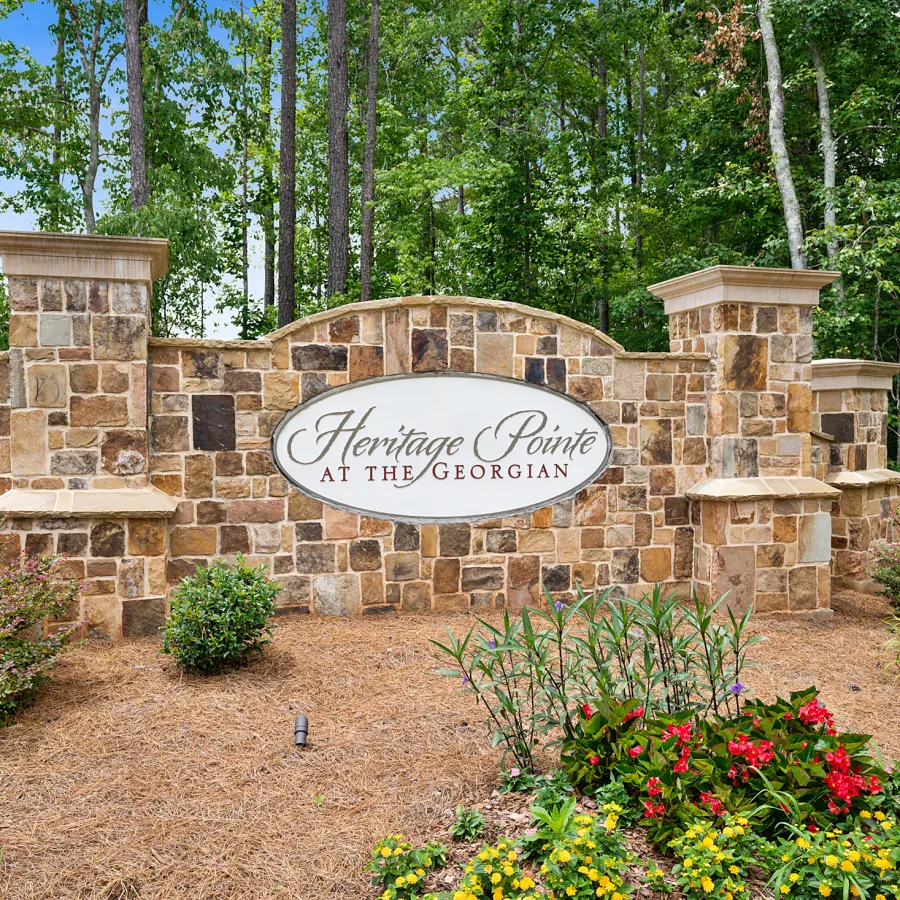 Stone entrance sign for Heritage Pointe at The Georgian surrounded by flowers and trees under a blue sky