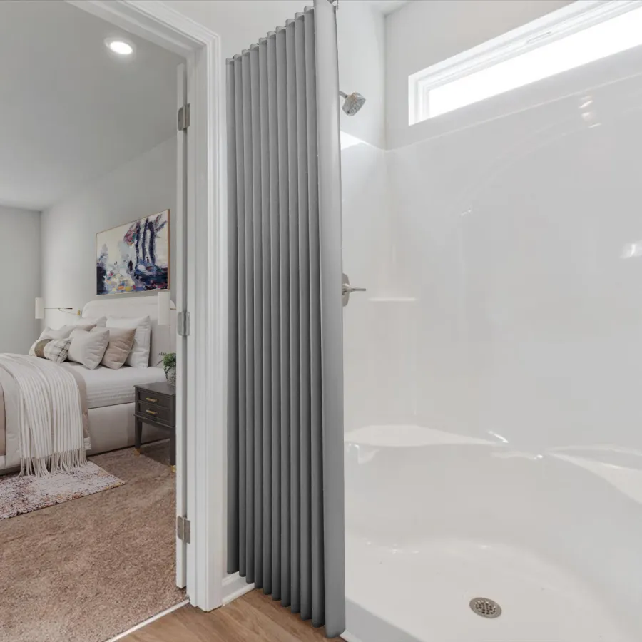 Modern bedroom with beige bedding adjacent to a white, clean bathroom shower area with a gray textured wall.