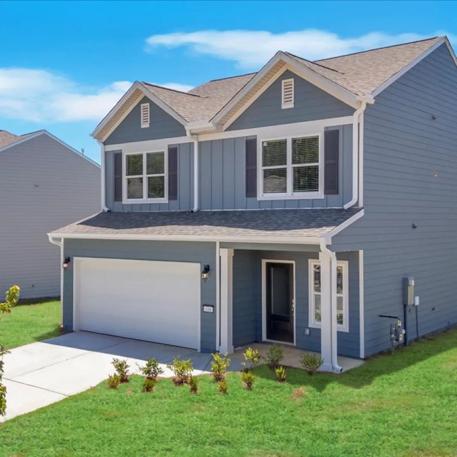 Modern two-story blue house with attached garage and manicured lawn under blue sky near a lake.