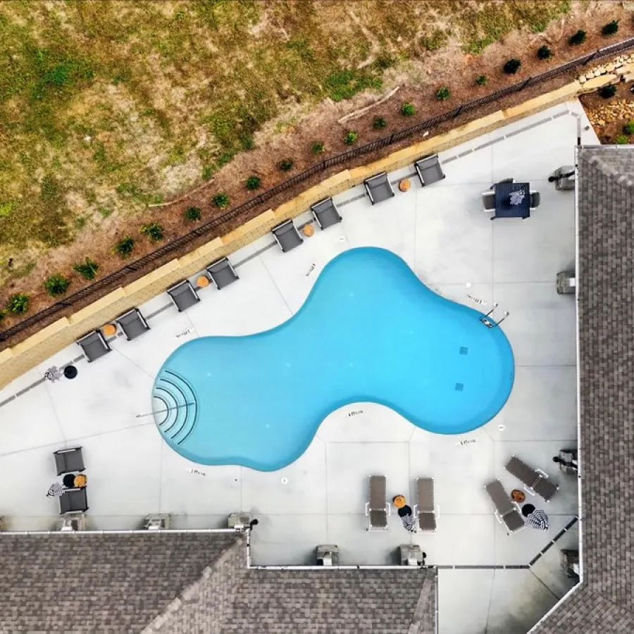 Aerial view of a kidney-shaped swimming pool surrounded by lounge chairs and buildings on a sunny day