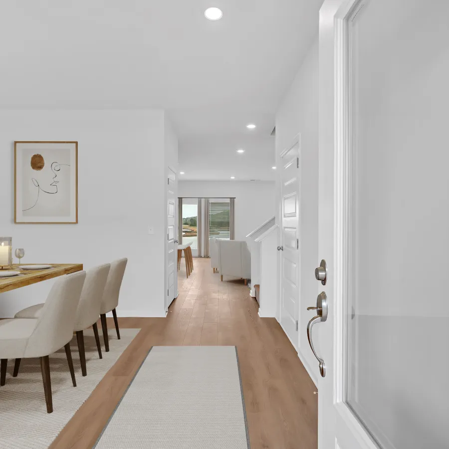Bright modern dining area with wooden table, beige chairs, artwork, and hallway leading to living room.