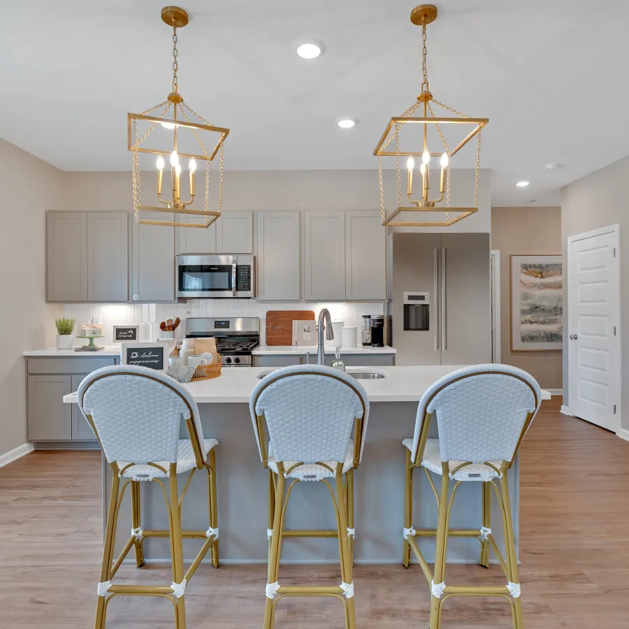 Modern kitchen with gray cabinets, white countertops, gold accents, and stylish bar stools.