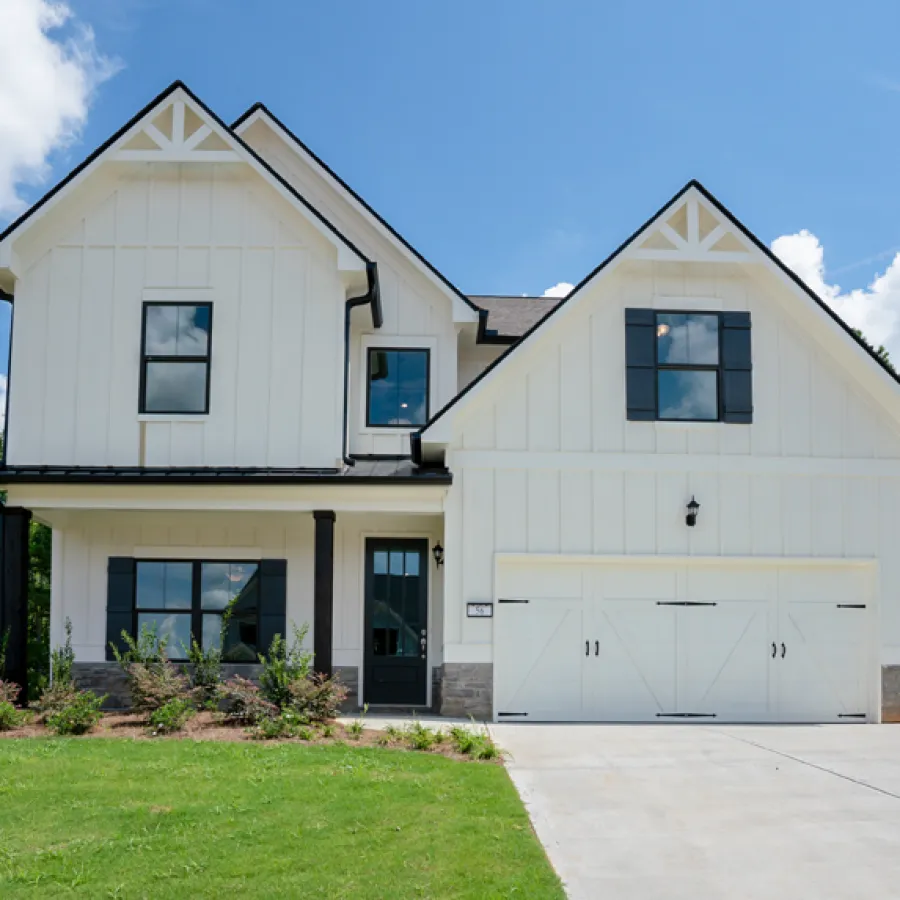 Modern two-story white house with black accents, large garage, front porch, and landscaped lawn under blue sky.
