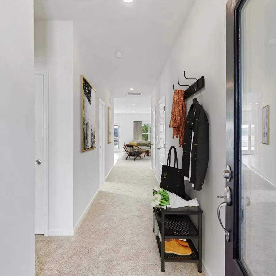 Bright hallway with carpet, wall art, coat hooks holding jackets and bags, and a bench with shoes.