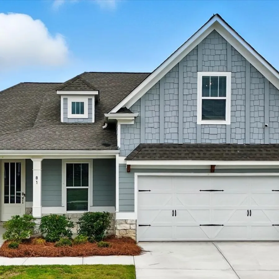 Modern two-story blue house with white garage door and neatly landscaped front yard under a blue sky.