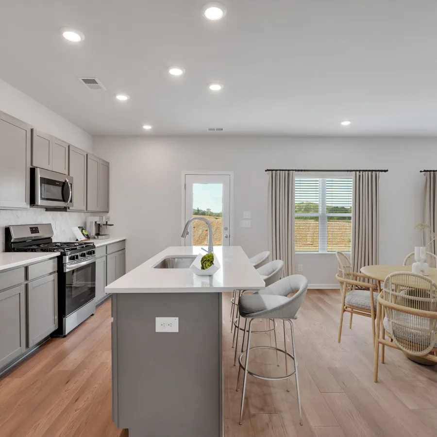 Modern kitchen with gray cabinets, white island, stainless steel appliances, and adjacent dining area with wooden chairs.