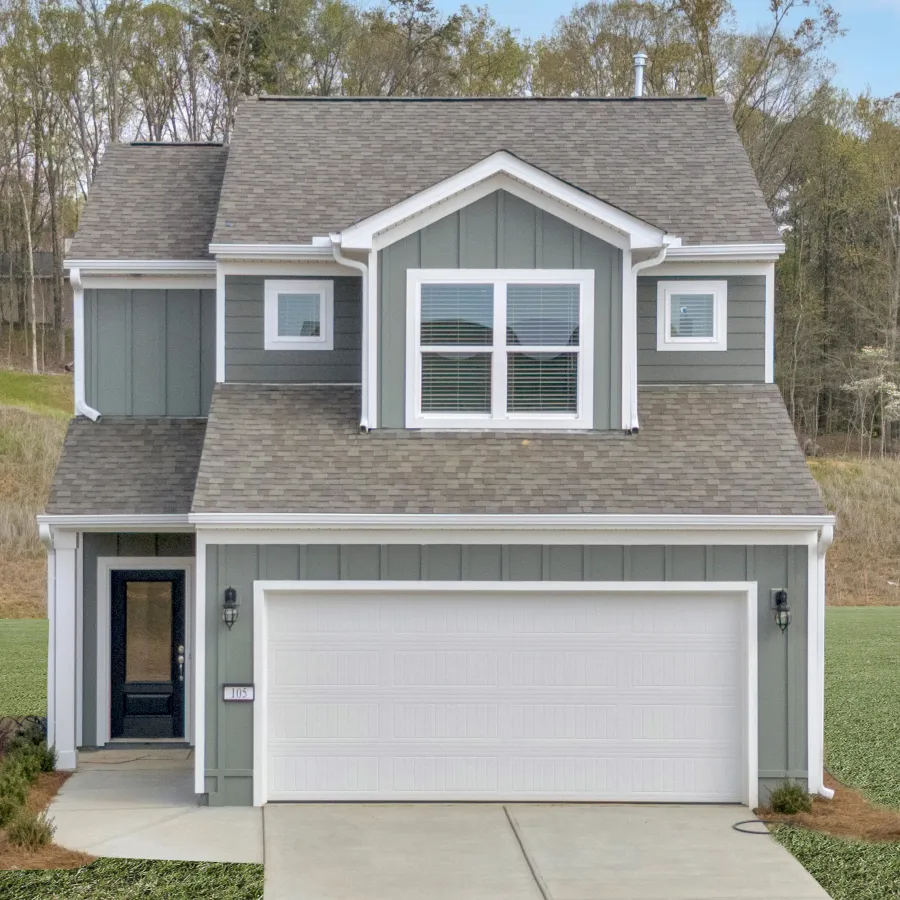 A modern two-story house with green siding, a white garage door, and landscaped surroundings.