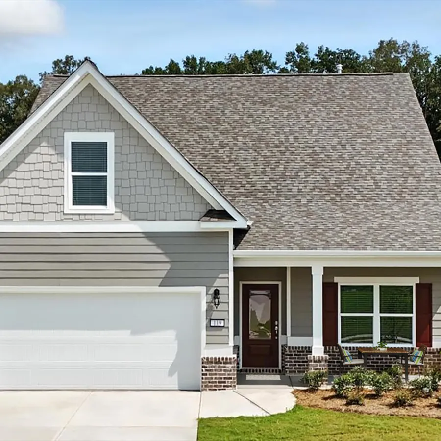 Modern gray suburban house with white garage door, front porch, and landscaped yard under blue sky.