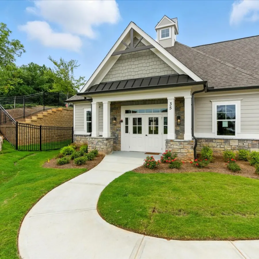Modern single-story building with stone accents, white doors, manicured lawn, and curved concrete pathway under clear sky