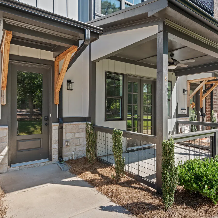 Modern townhouse exterior with stone and siding facade, covered porch, and small landscaped yard under blue sky.