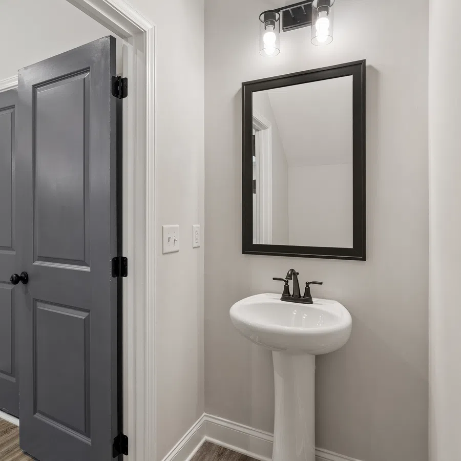 Modern bathroom with pedestal sink, black framed mirror, black faucets, and gray double doors.