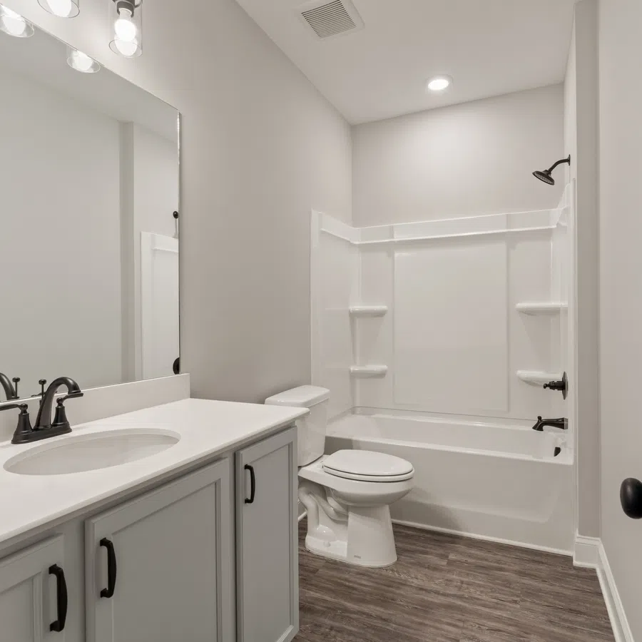 Modern bathroom with white vanity, black fixtures, bathtub-shower combo, and wood-look flooring under bright lighting