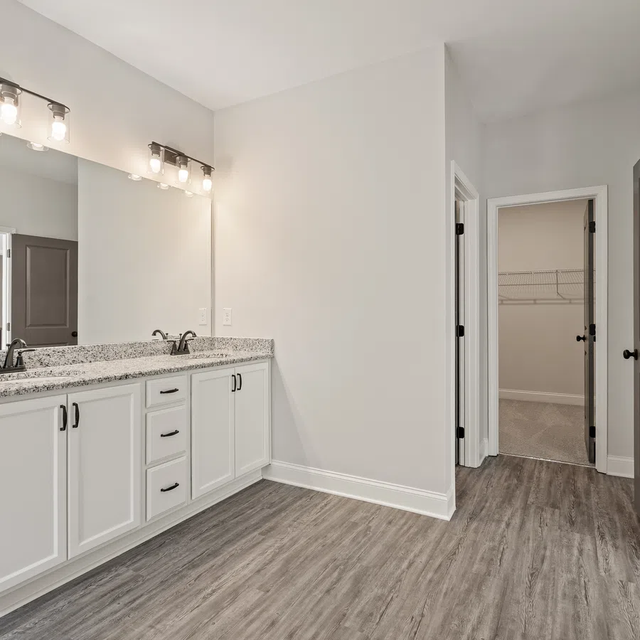 Modern bathroom with double vanity, granite countertops, large mirror, gray flooring, and adjacent walk-in closet.