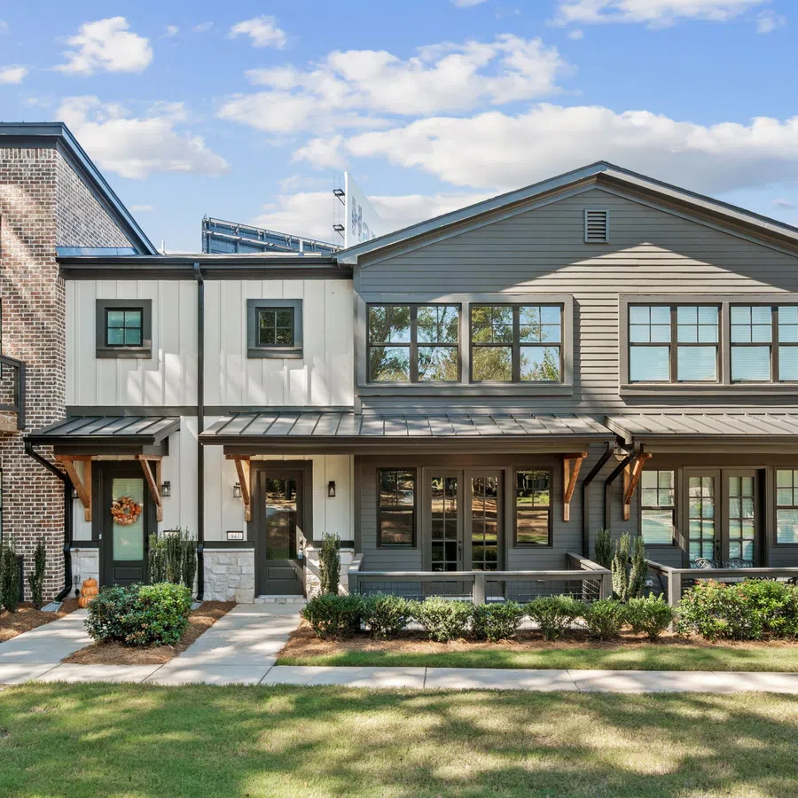 Modern townhouse complex with brick and siding exteriors, large windows, and green landscaping under a blue sky.