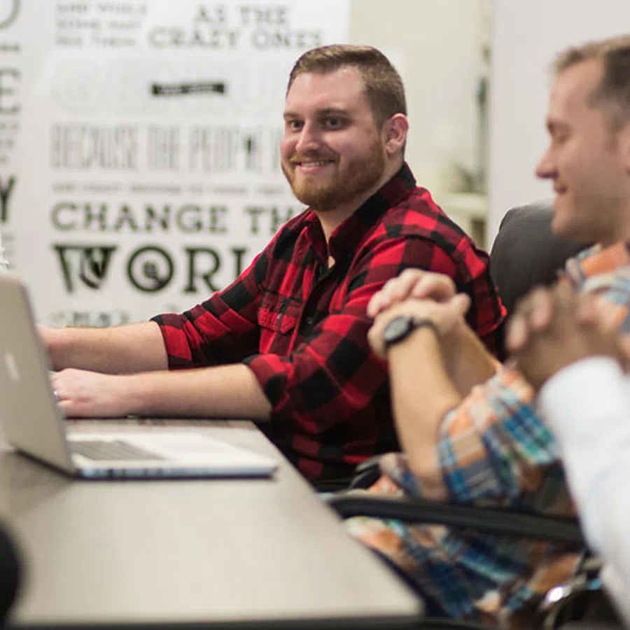 Four men having a meeting around a table with laptops in a modern office setting with motivational wall art.
