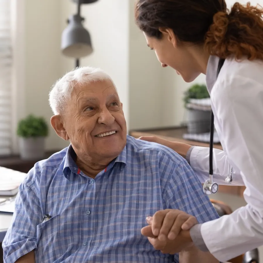 Doctor holding hands and smiling with elderly male patient in a bright medical office