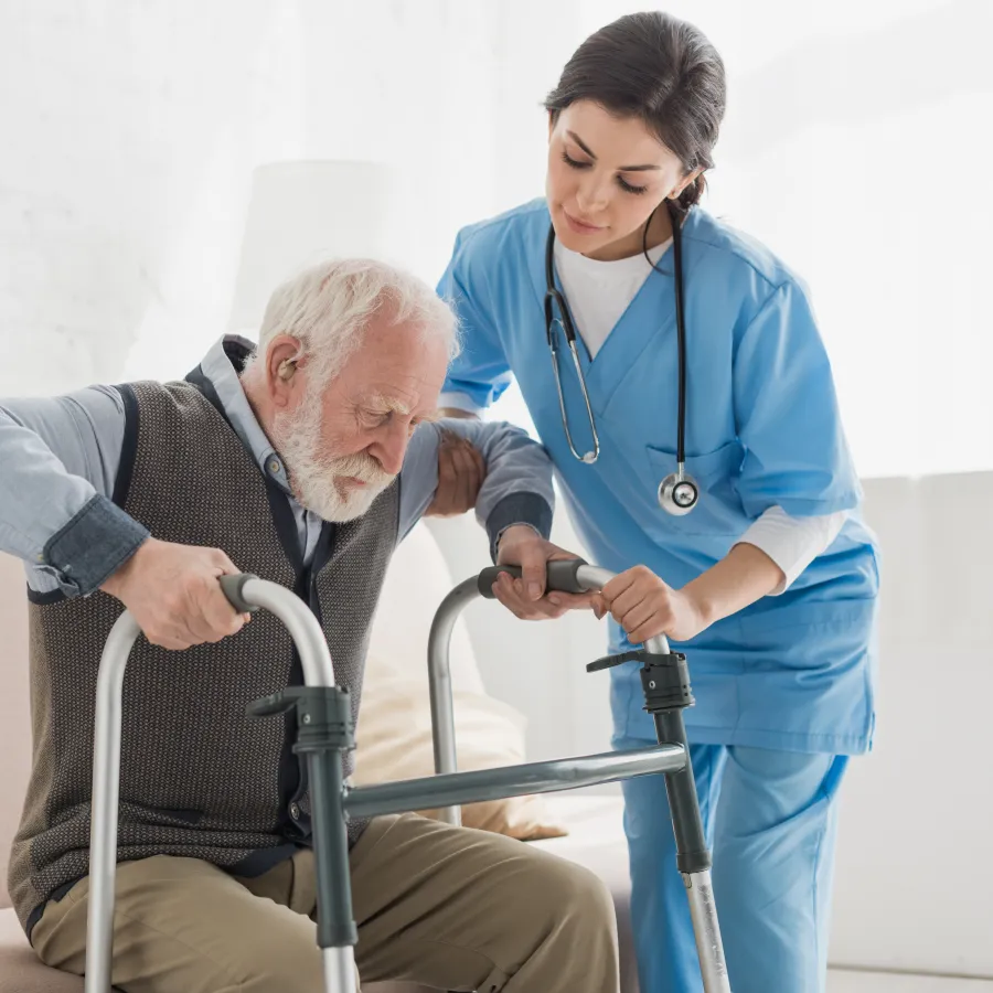 Nurse assisting elderly man with walker as he stands up from couch in bright room.