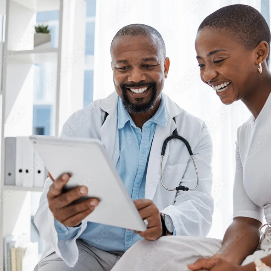 Smiling doctor showing medical information on tablet to happy female patient in bright clinic.