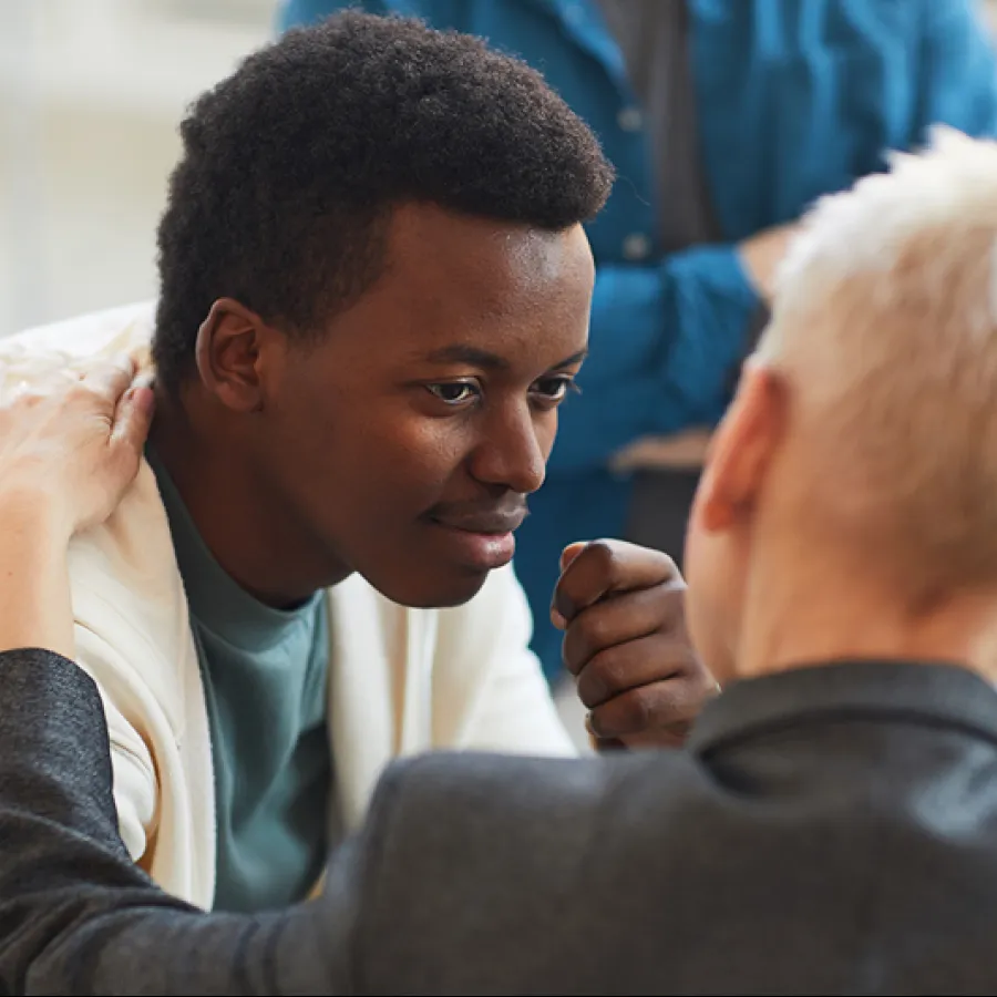Young man in white hoodie receiving support from a blonde person in gray jacket during a conversation.
