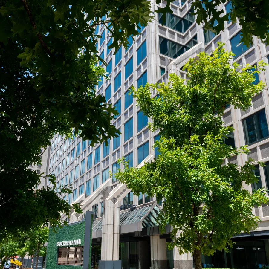 Modern office building with glass windows surrounded by green trees on a sunny day