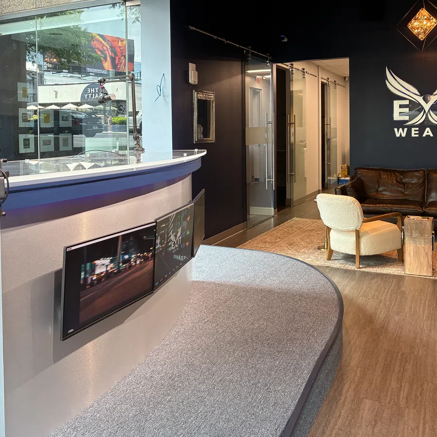 Modern office lobby with curved reception desk, monitors, leather sofa, chairs, and Exit Wealth logo on dark wall.
