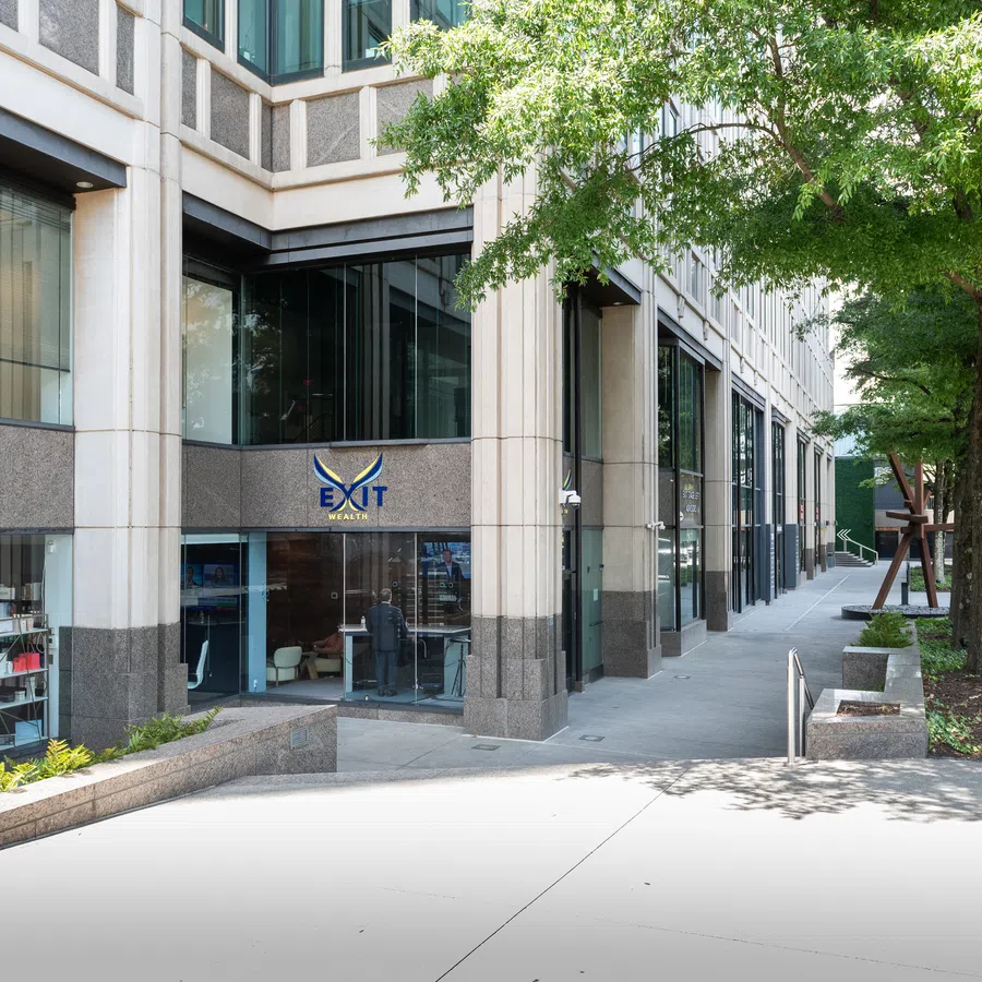 Urban street with Exit Realty office in a modern commercial building and trees lining the sidewalk on a sunny day