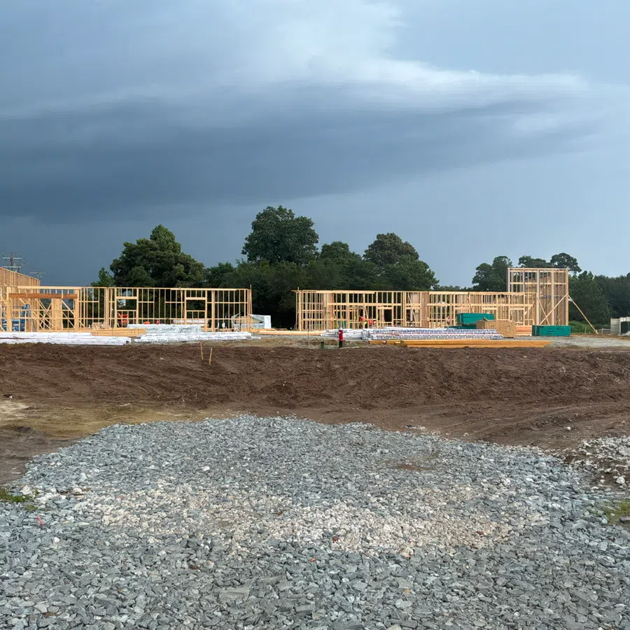 Partially framed wooden structures at a construction site under a cloudy sky with gravel and dirt foreground.