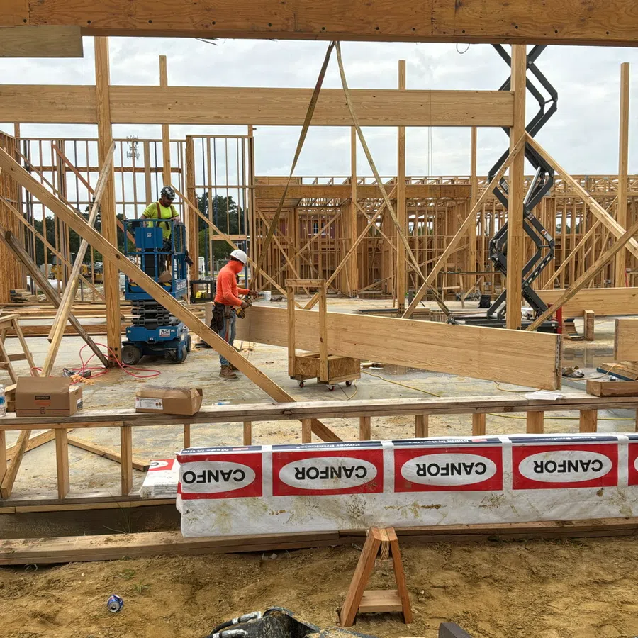 Construction site with workers assembling wooden framing and beams for a building structure under cloudy sky.