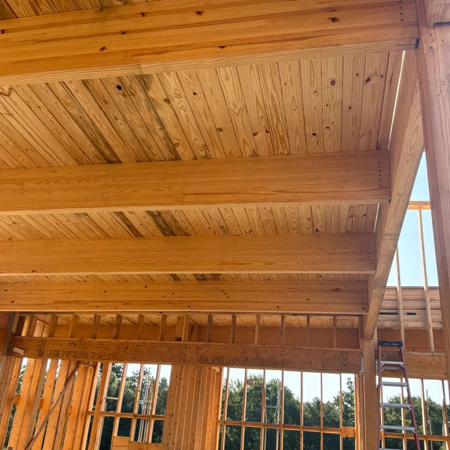 Interior view of wooden frame construction showing beams, ceiling, and wall studs in a building under construction.