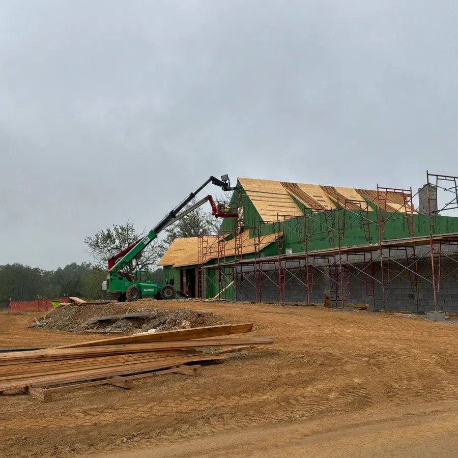 Partially constructed building with scaffolding and a green boom lift on a dirt construction site under cloudy sky
