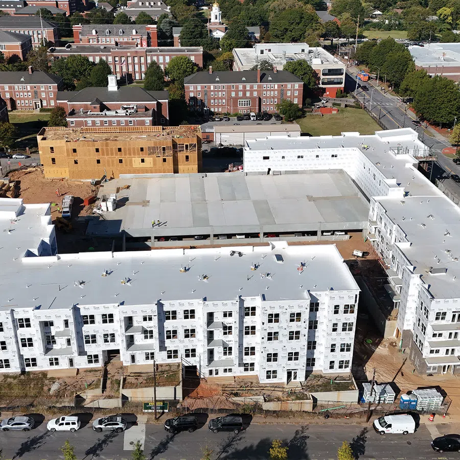 Aerial view of a large white multi-story residential building under construction in an urban area with surrounding streets.